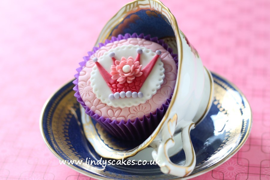 Beautifully detailed crown decorates the top of this pretty pink princess cupcake displayed in a teacup