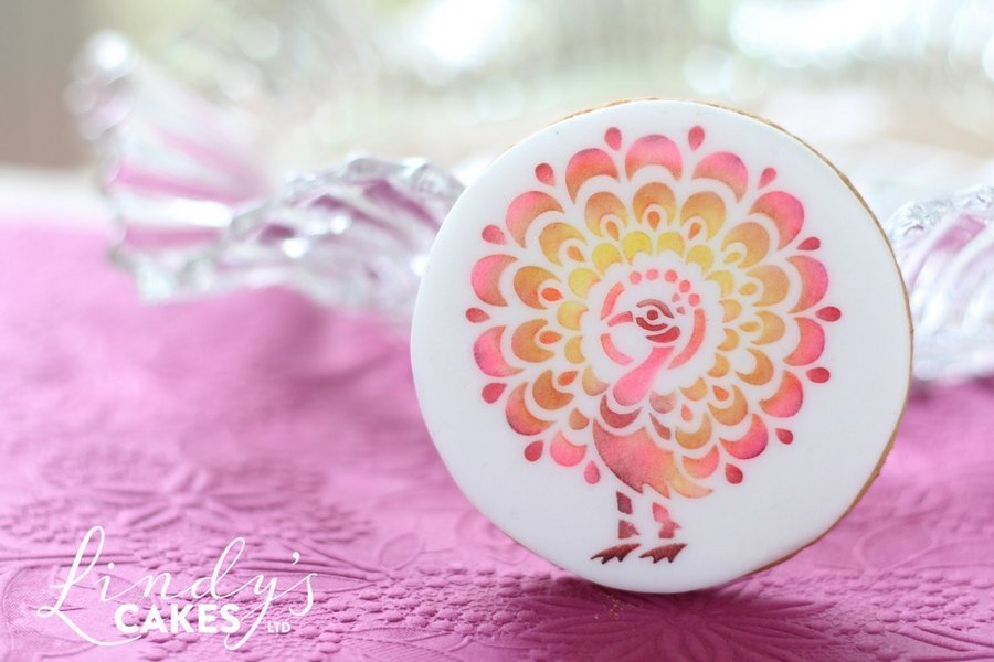 Pink peacock stencilled onto a sugarpaste covered biscuit